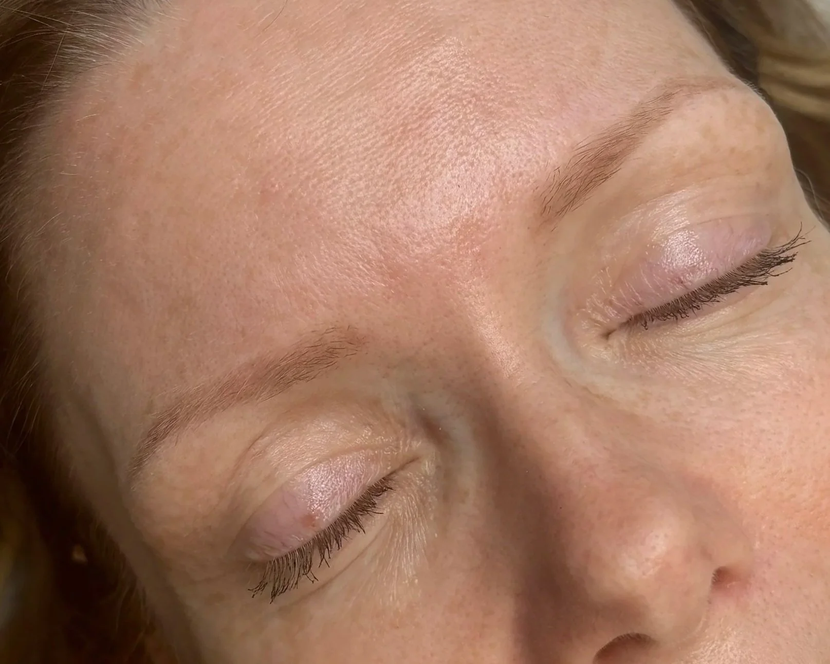Close-up of a woman's face with closed eyes, showcasing smooth skin, eyebrows, and eyelashes.