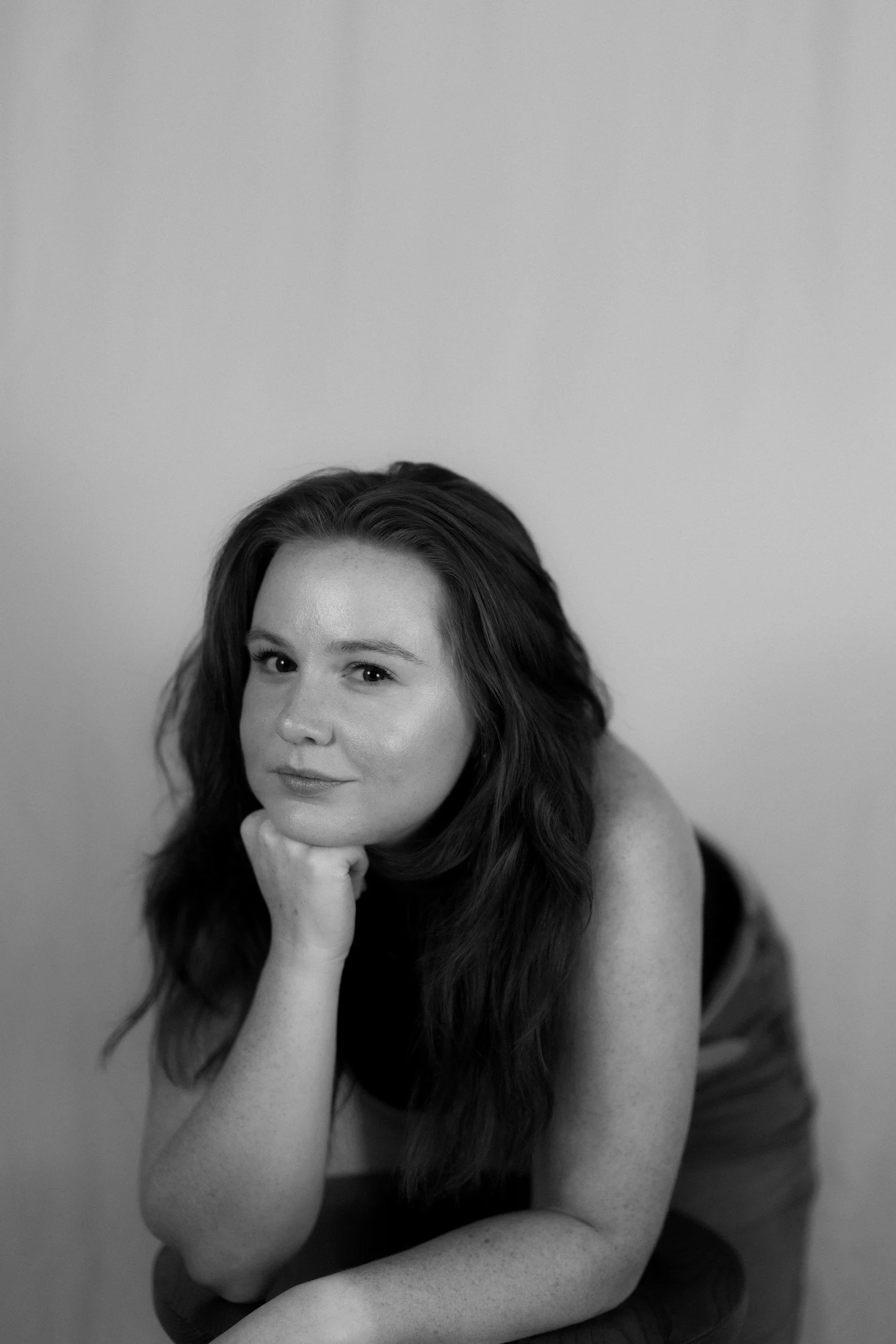 A woman with long hair leans forward, resting her chin on her hand, reflecting on psychotherapy for women in Miami.
