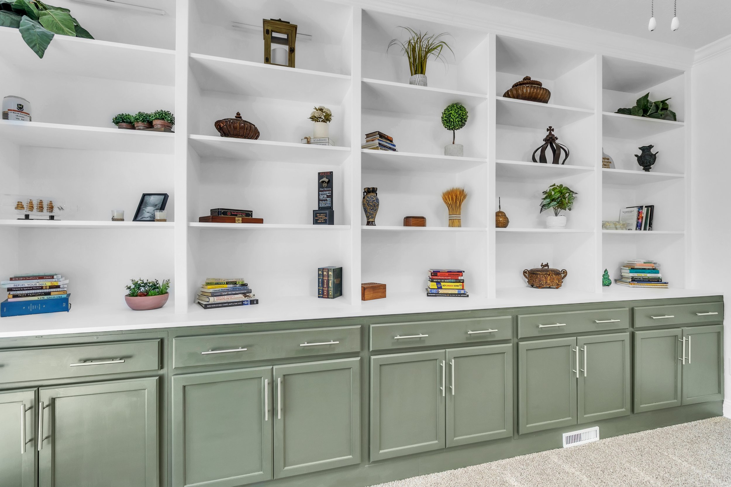 A white built-in bookshelf with decorative items and books on the shelves, and green cabinetry below.