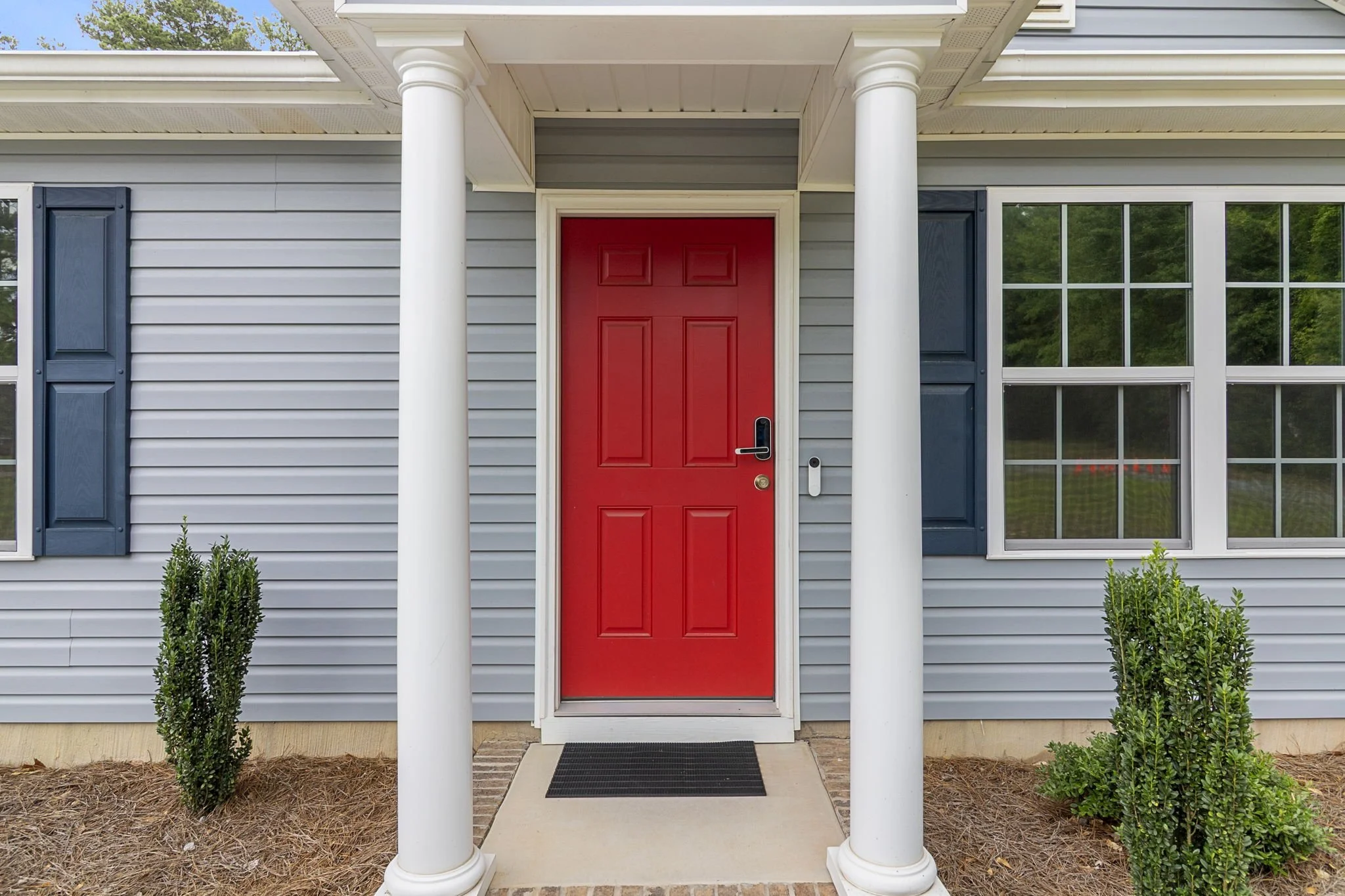 Front porch of a house with a red door, white columns, and blue window shutters.