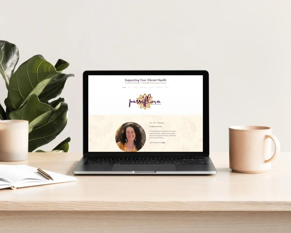 Laptop showing client website on table with notebook, mug, and houseplant