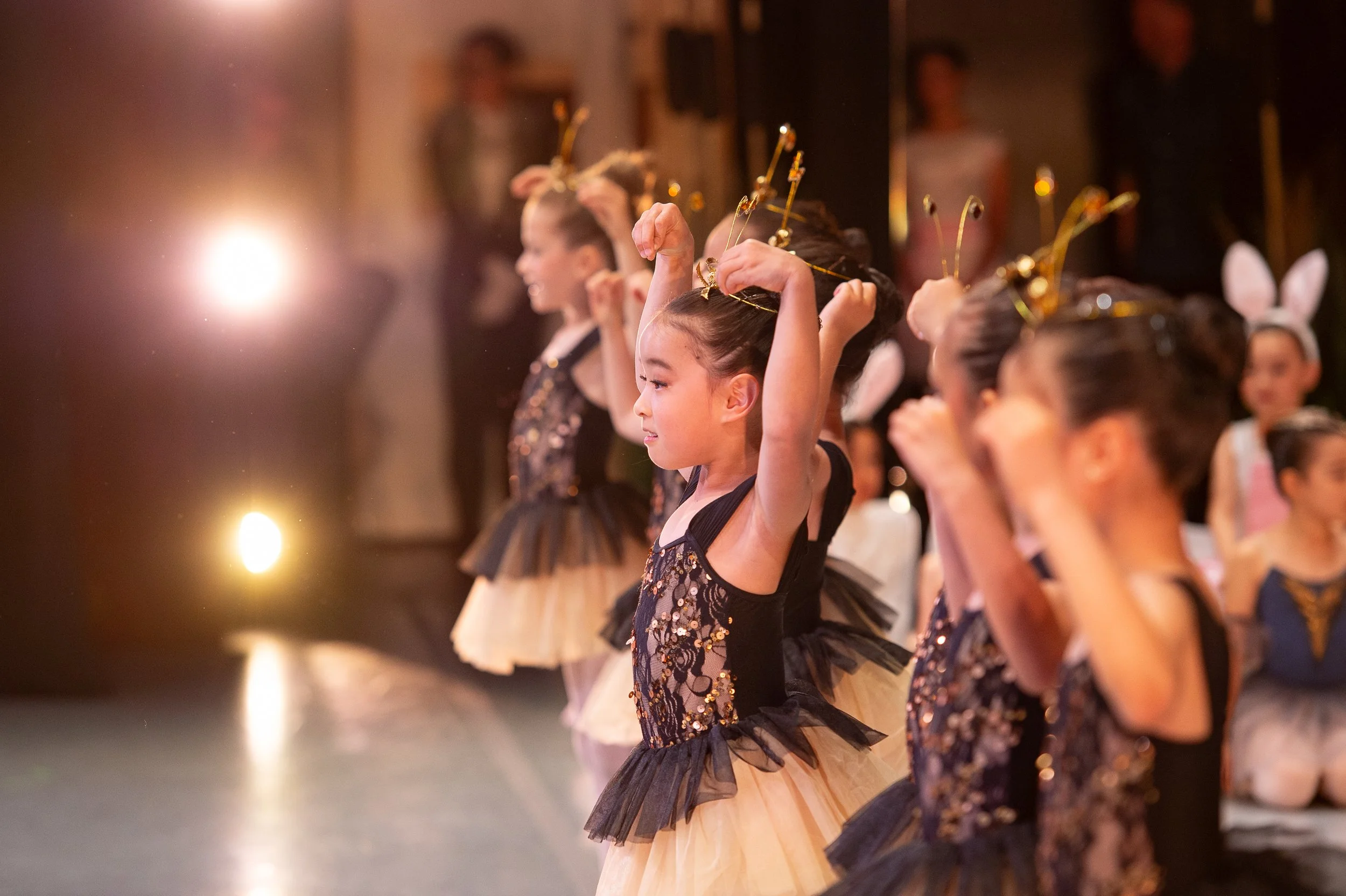 Young girls dressed in ballet costumes practicing ballet on stage.