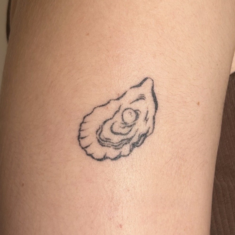 A tattoo of an oyster shell with a pearl inside on the arm