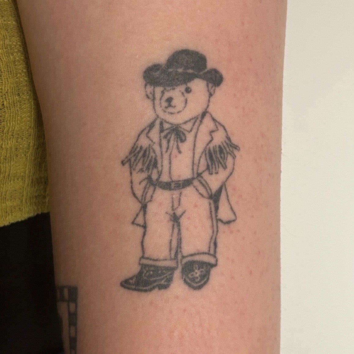Tattoo of a bear dressed as a cowboy on the upper arm