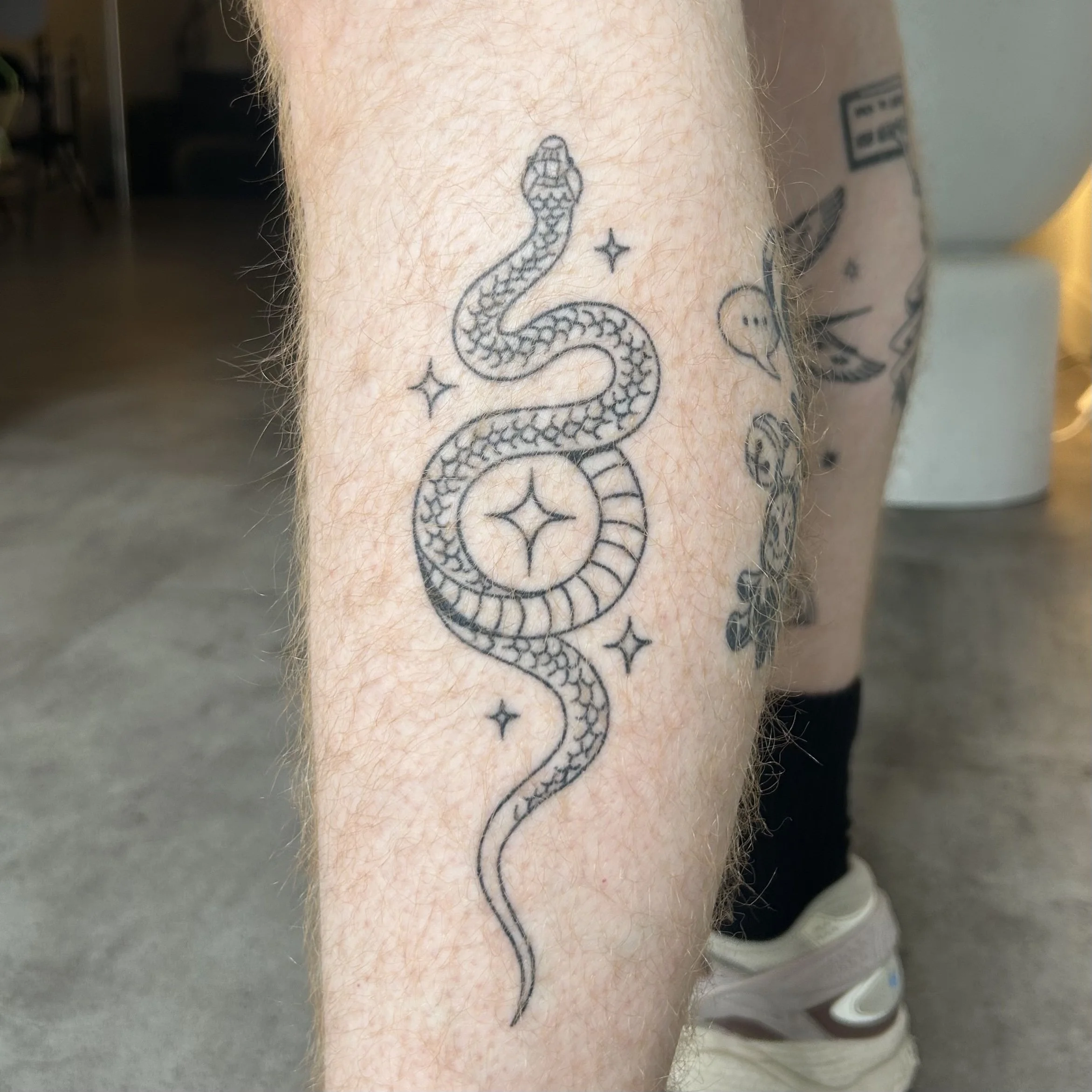 Tattoo of a snake that forms a circle with stars on the leg