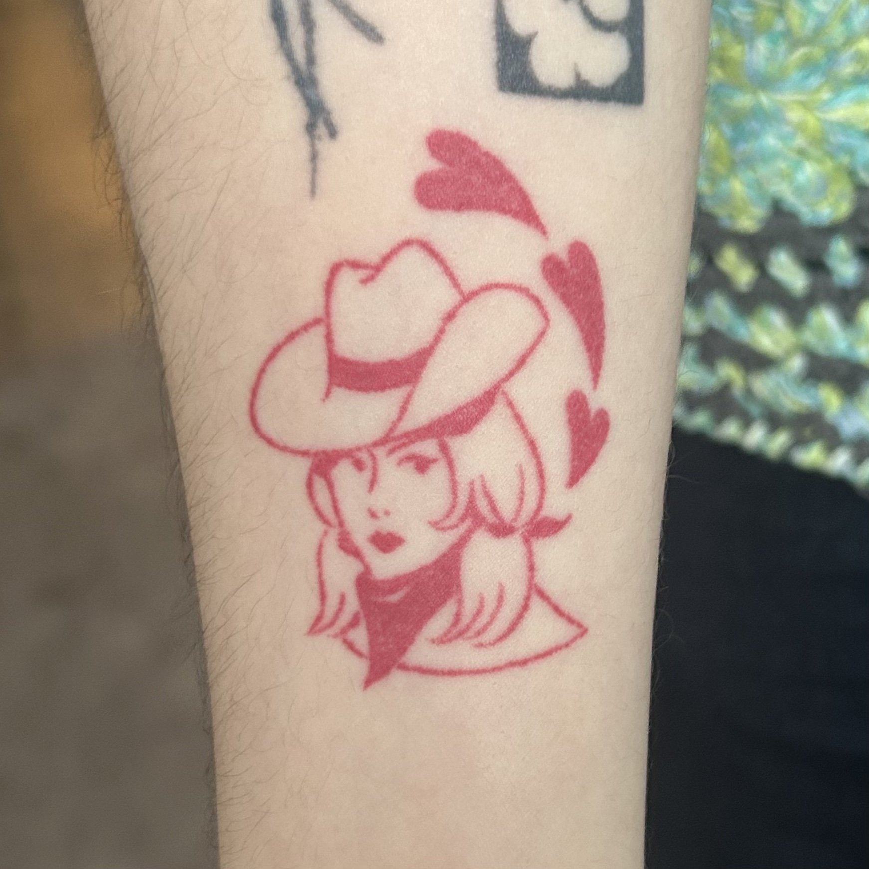 Red tattoo of a cowgirl wearing a cowboy hat with hearts around her head on the arm