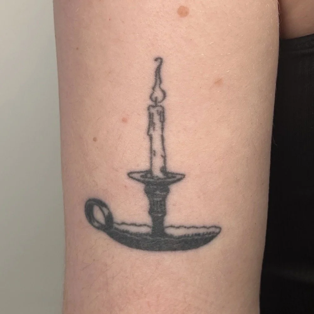 A tattoo of a candlestick holder with a lit candle on top on the upper arm