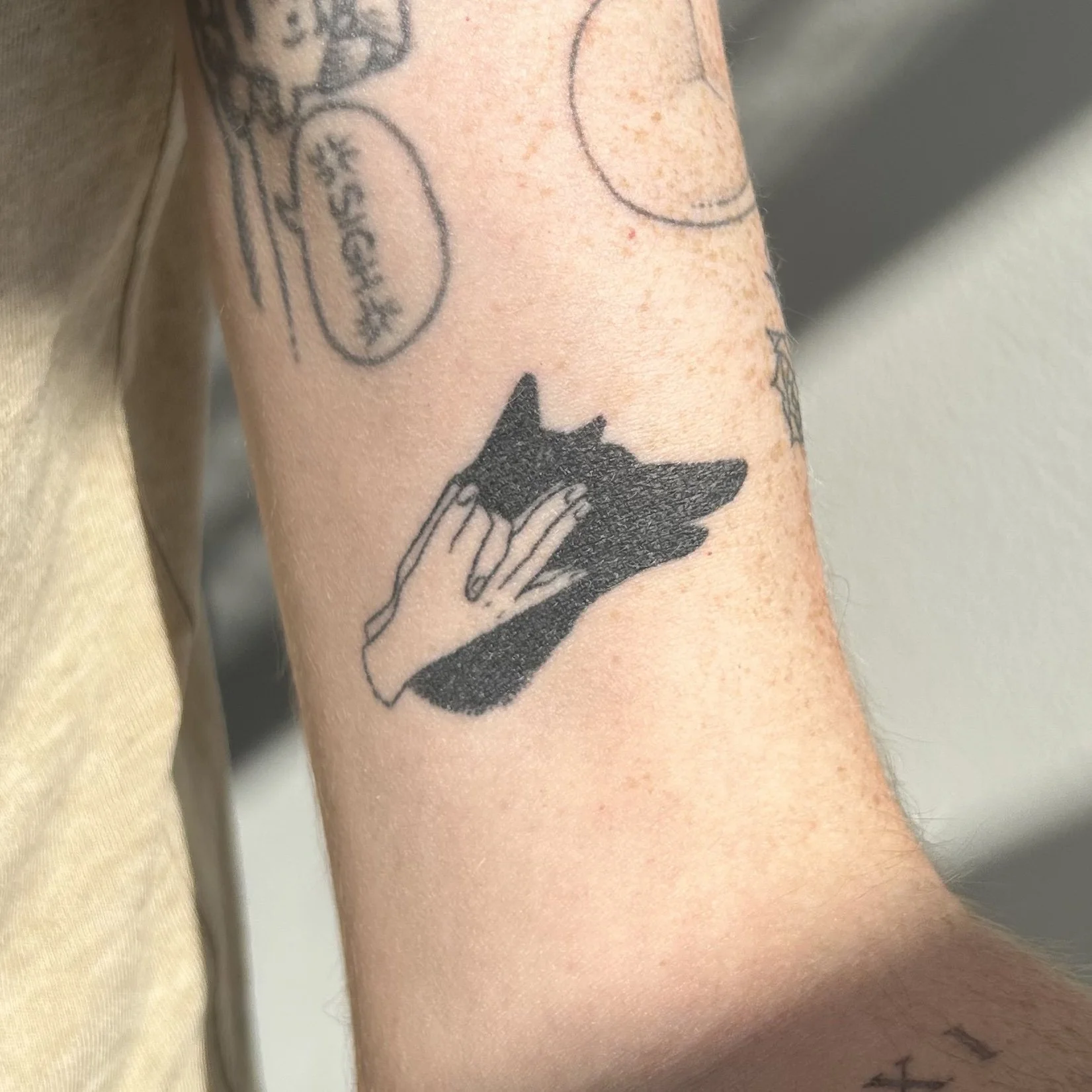Tattoo of a hand creating a shadow of a dog's head on the arm