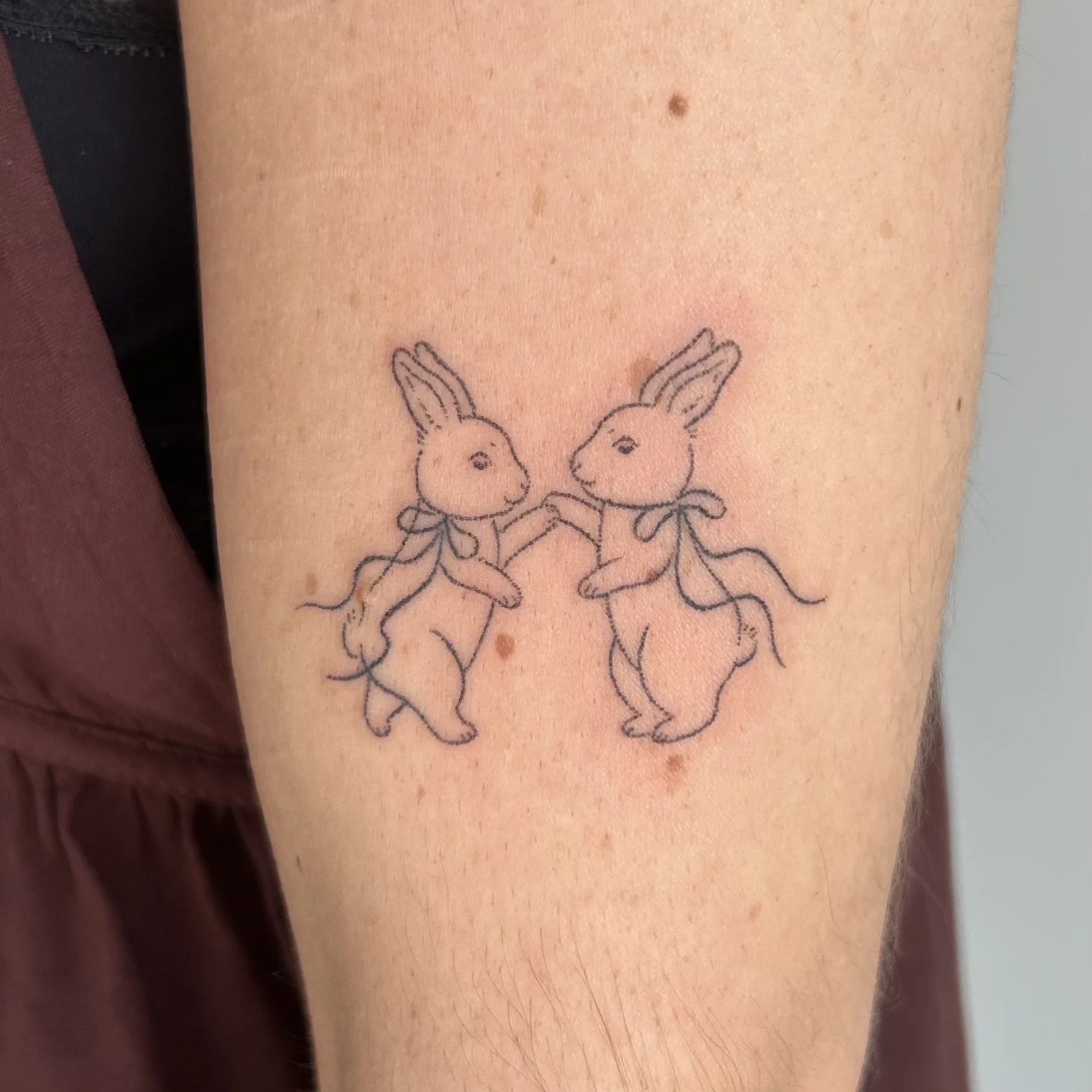 Tattoo of two rabbits wearing bows and holding hands on the upper arm