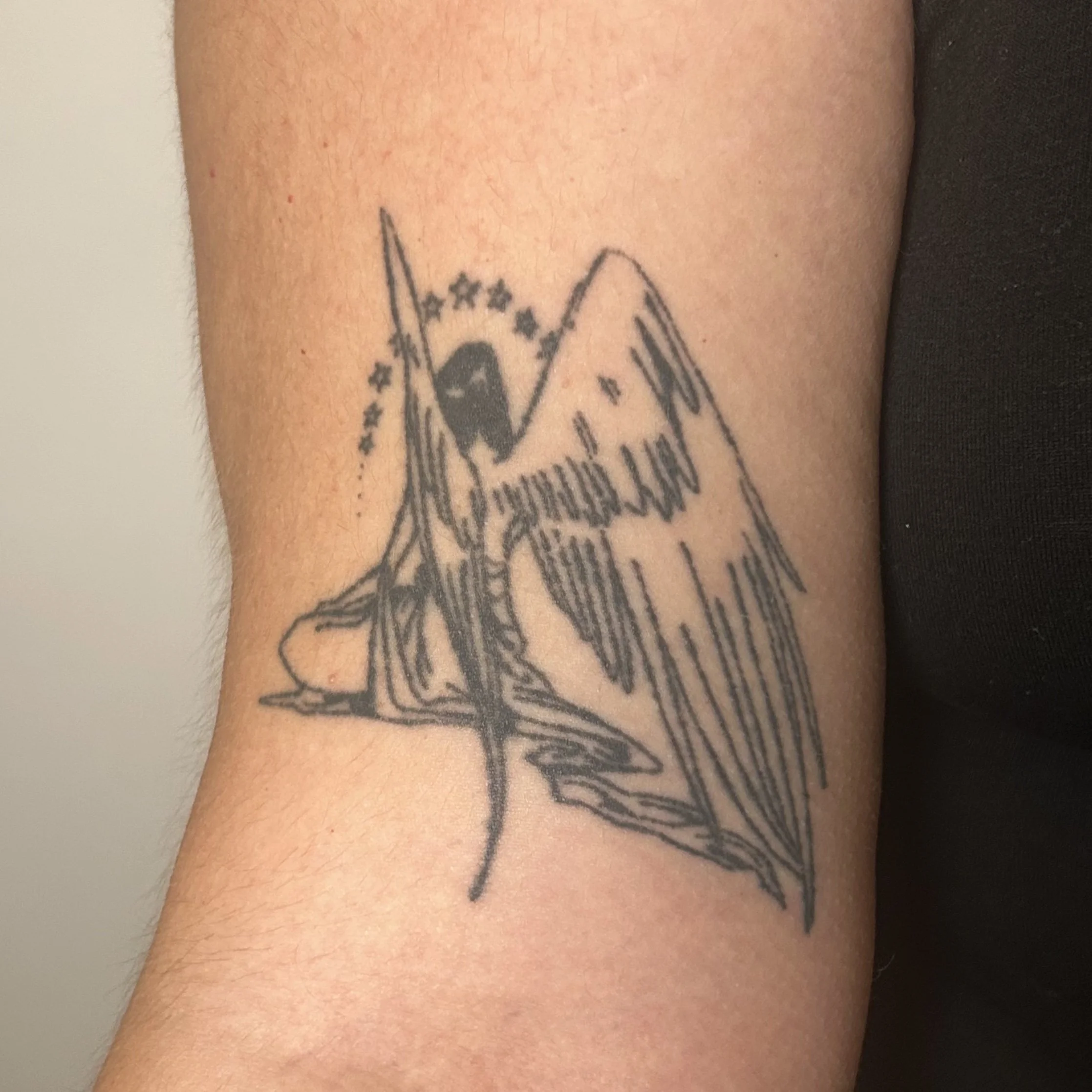 Tattoo of the backside of angel sitting with an arc of stars above
