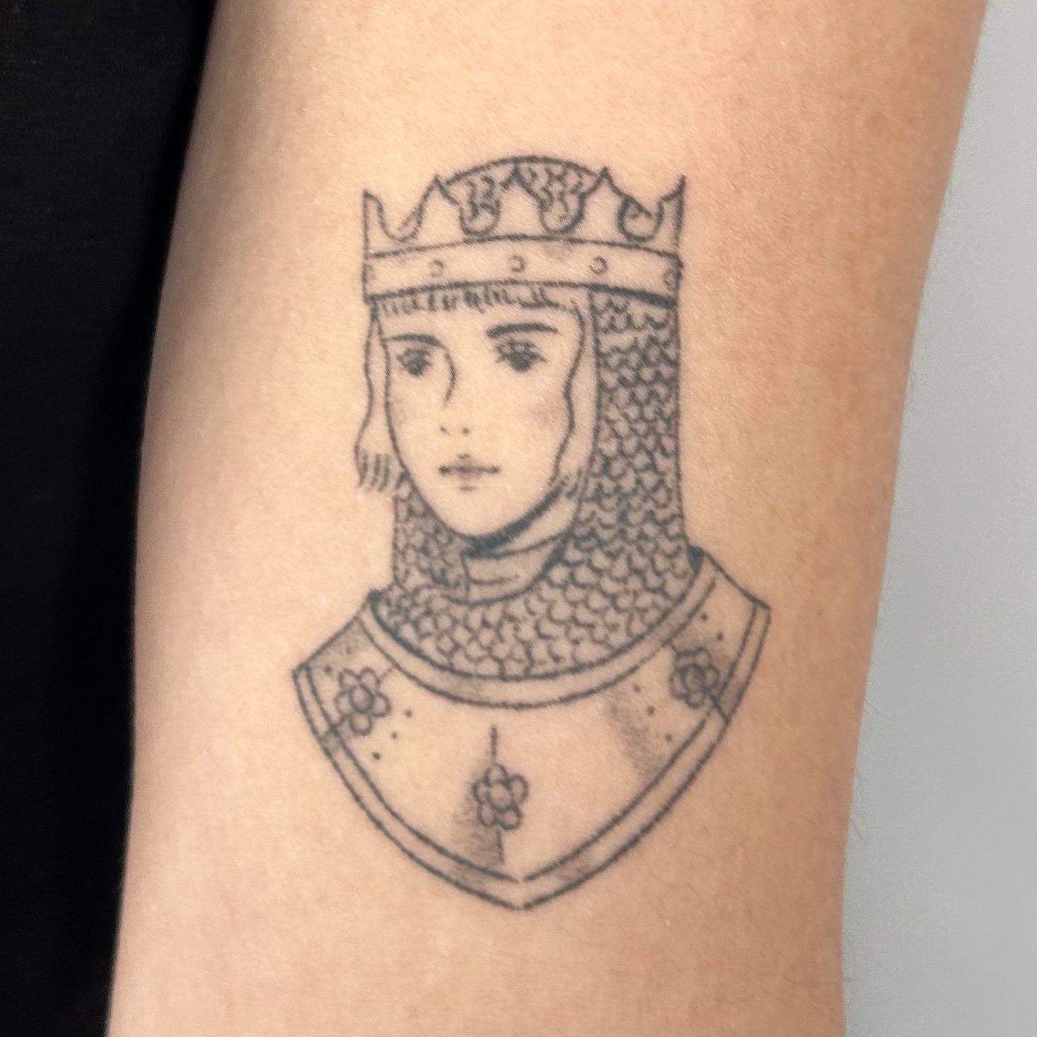 Tattoo of a female knight wearing a chainmail coif and crown on the upper arm