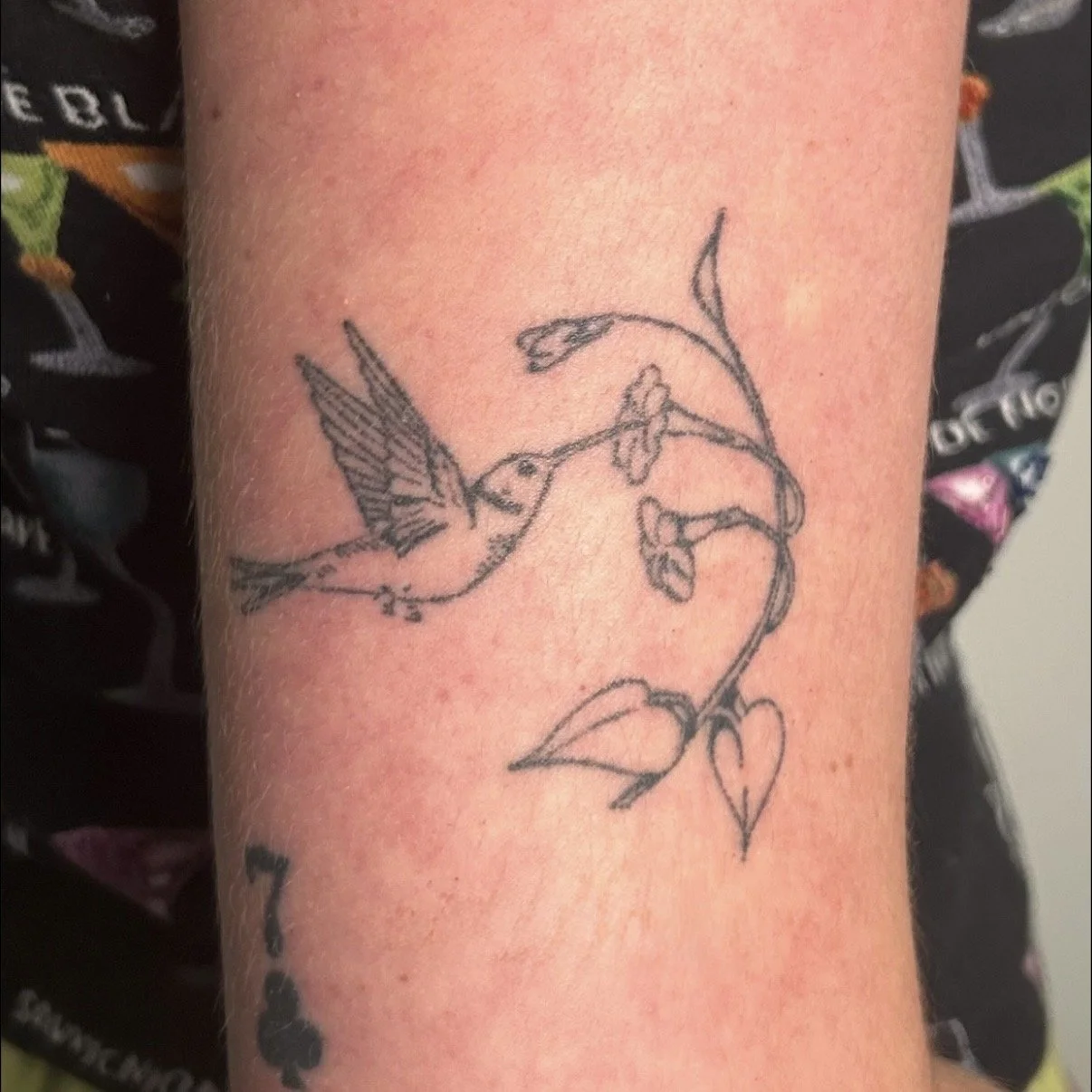 Tattoo of a hummingbird eating from a flower branch on the arm