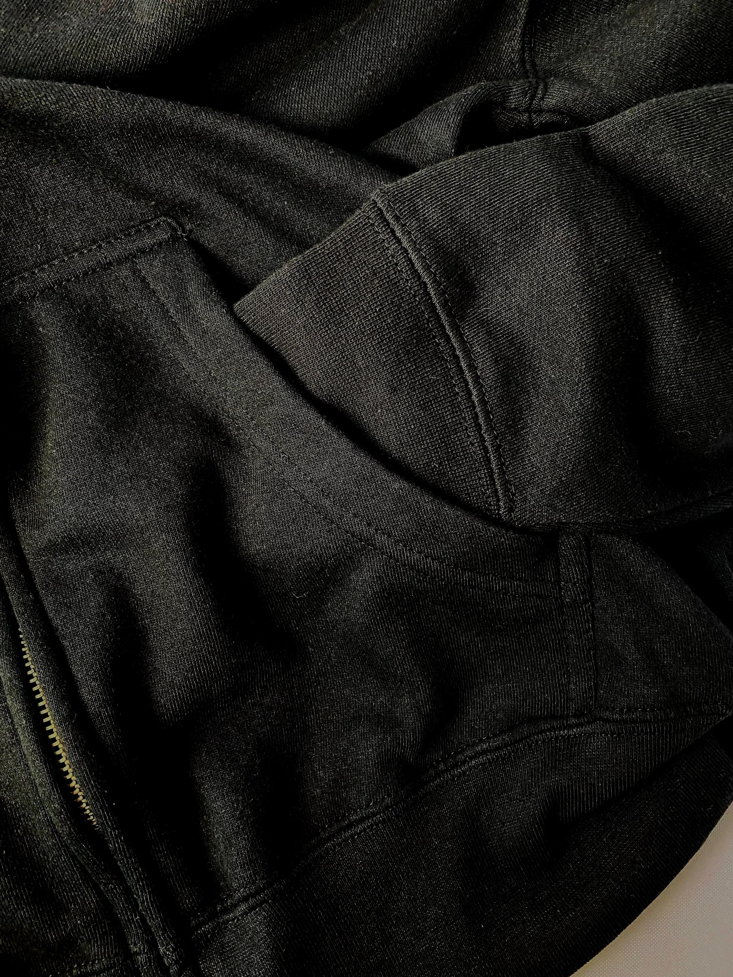 close up of the restless breeds black zip up hoodies cuff and pocket of sweatshirt