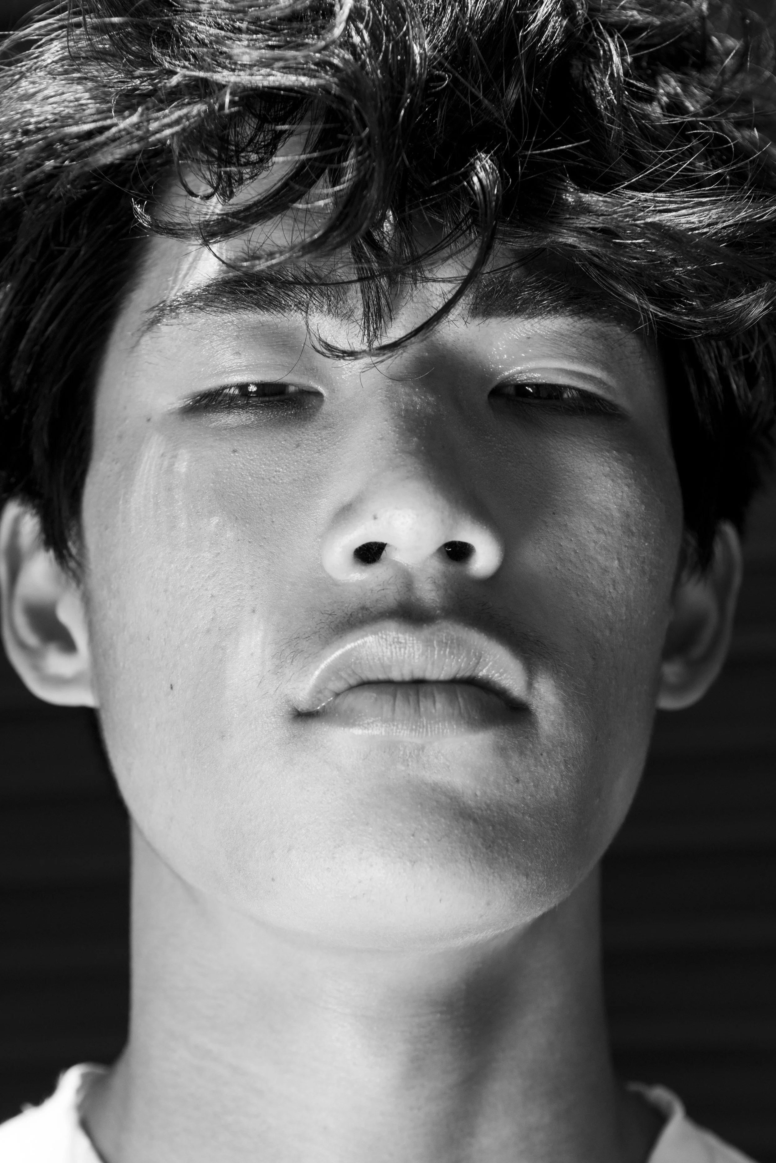 Close-up black and white portrait of a young person with messy hair, slightly closed eyes, and relaxed lips.