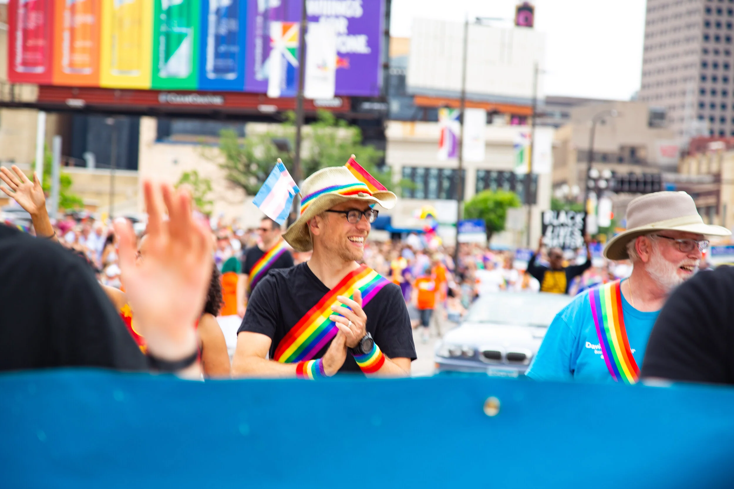 People participating in a pride parade, wearing rainbow accessories, and waving rainbow flags.