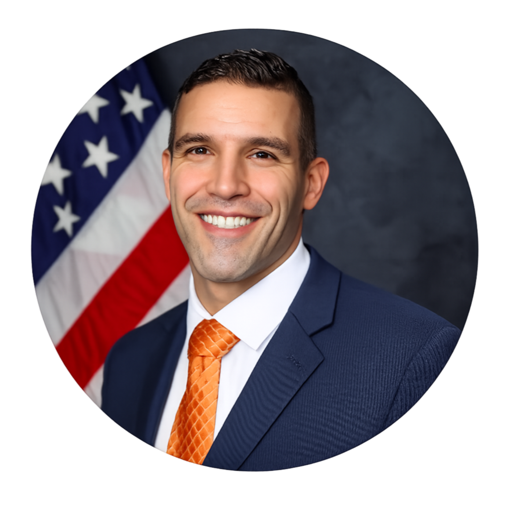 Noam Oz, defense advisor, in a dark blue suit, white shirt, and orange tie, smiling in front of an American flag.