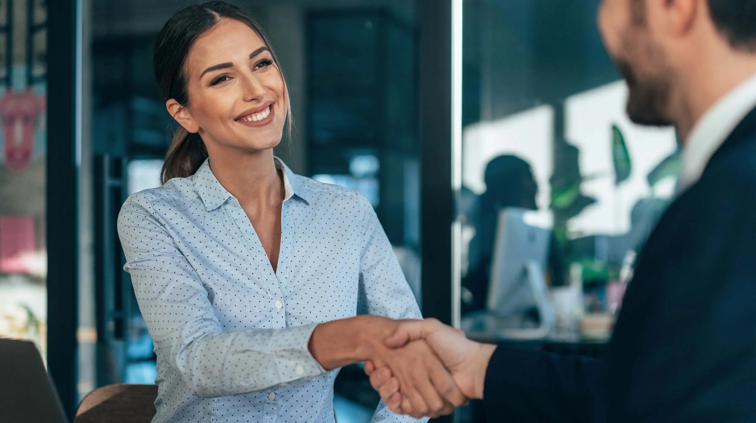 A woman smiling and shaking hands with a man in an office setting.