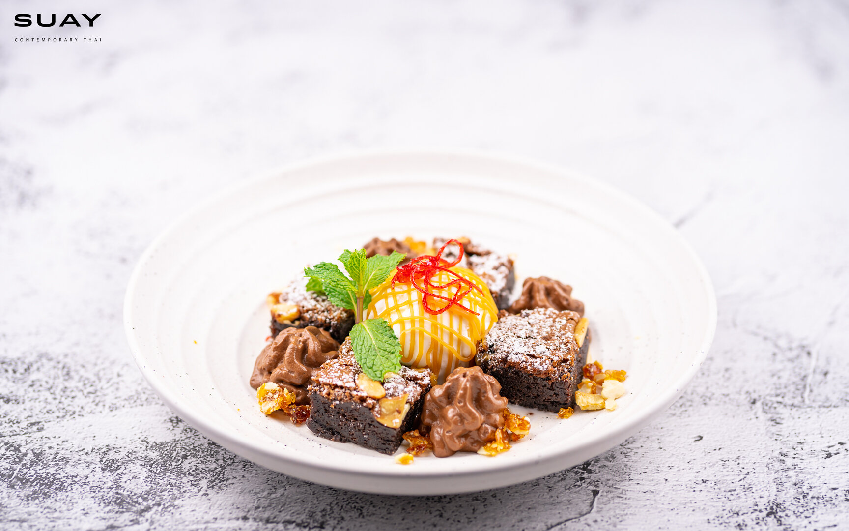 Homemade cashew nut brownie with salted caramel sauce served with young coconut ice cream.