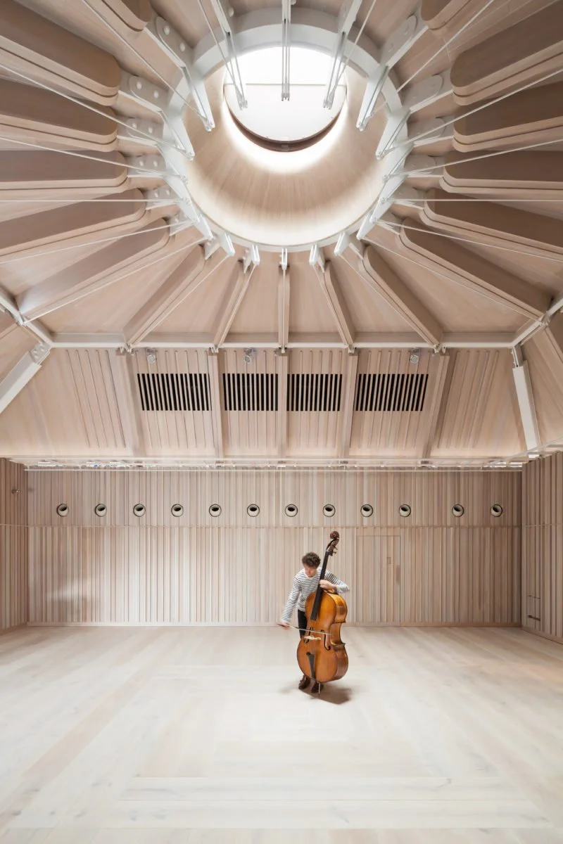 Royal Academy of Music. Angela Burgess Recital Hall. A student playing a double bass in a spacious, wooden music recital hall / rehearsal studio with high ceilings and natural lighting.