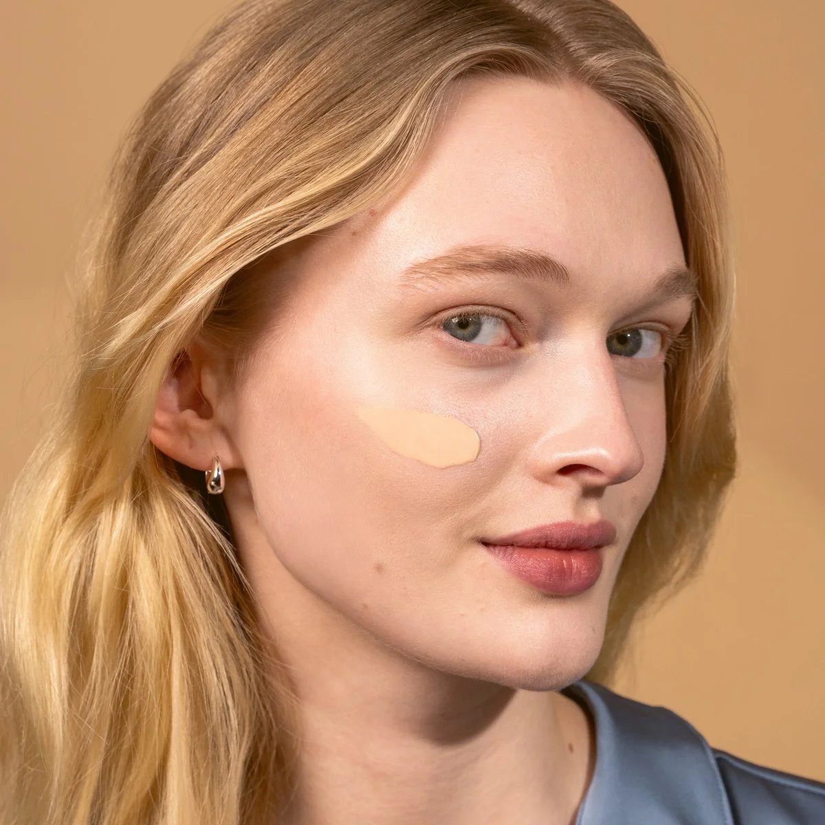 A young woman with blonde hair applying foundation to her face.