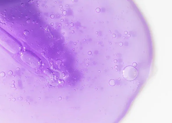 Close-up of a purple liquid with bubbles and a dropper submerged in it.