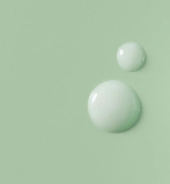 Two white drops on a light green surface, with the larger drop below and to the left of the smaller one.