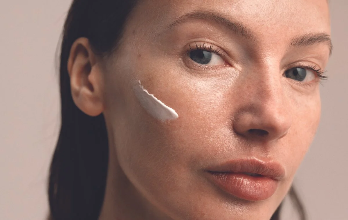 Close-up of a woman applying facial cream to her cheek.