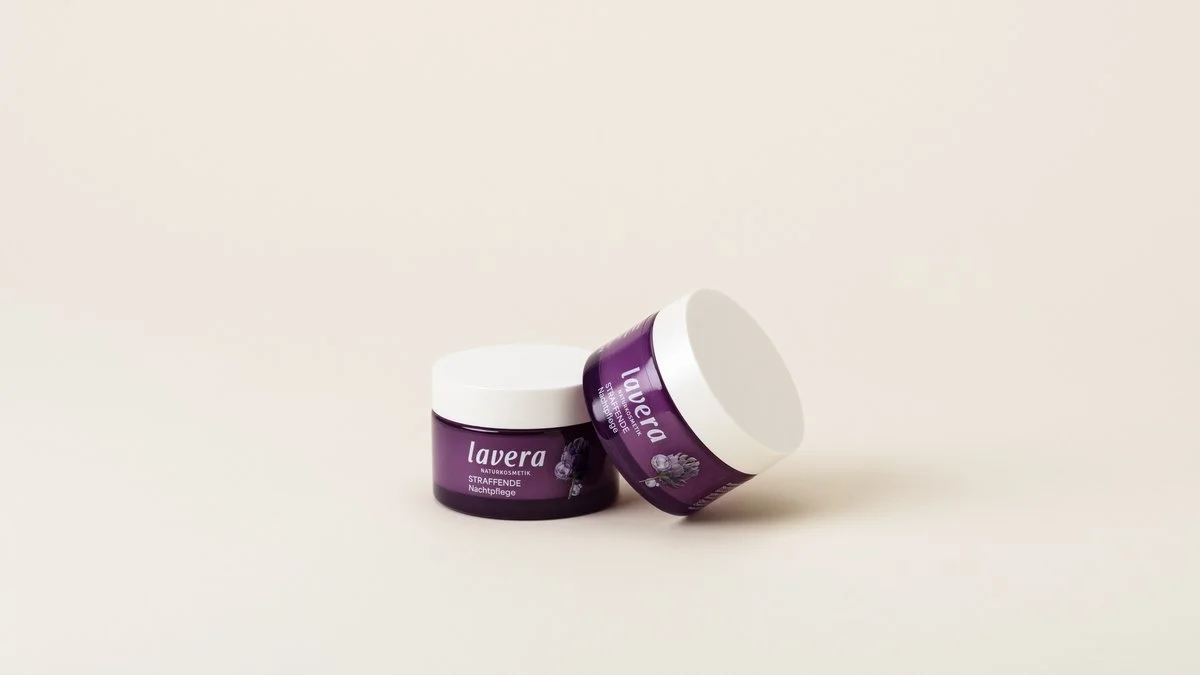Two purple jars of lavera Firming Night Cream on a beige surface, one jar standing upright and the other tilted.