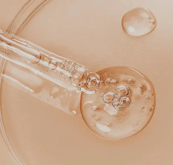 Close-up of a pipette adding a clear liquid to a petri dish with bubbles.
