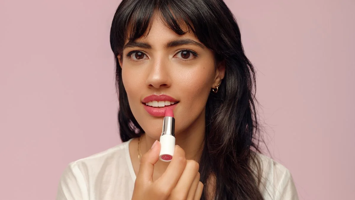 Woman applying pink lipstick against a light pink background
