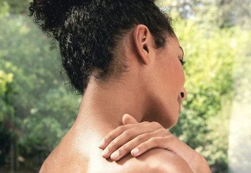A woman with natural curly hair touching her shoulder.