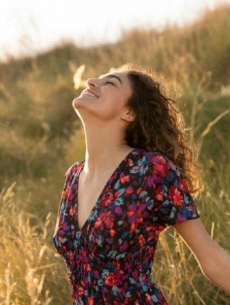 Woman smiling with arms outstretched in a grassy field during sunset.