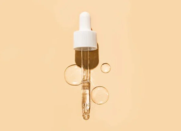 A clear dropper filled with a transparent liquid, with three air bubbles around it, set against a beige background.