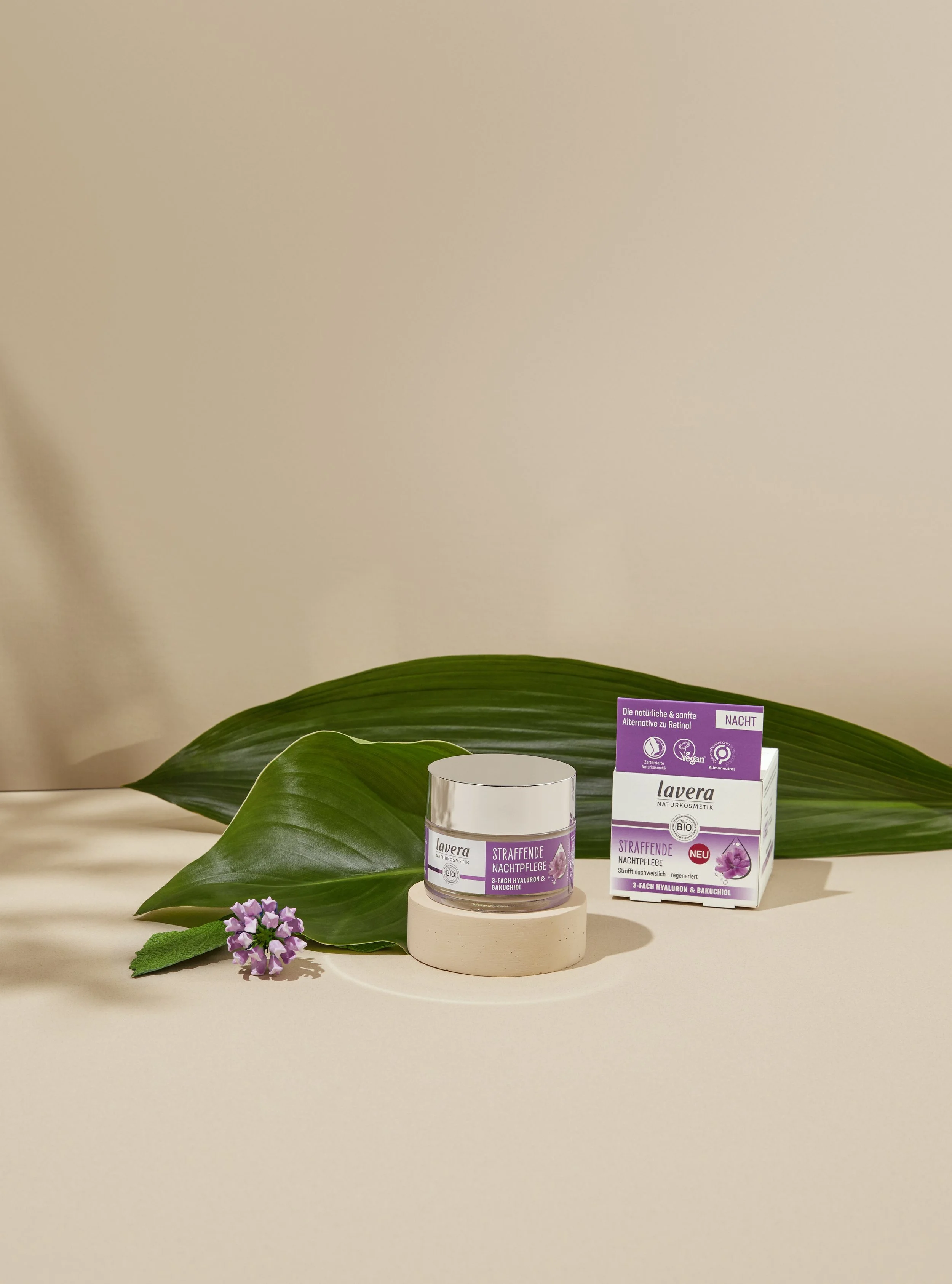 lavera Firming Day Cream product with large green leaf, small purple flowers, and product packaging on a beige surface.