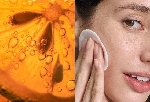 Close-up of a woman using a cotton pad to wipe her face, with a background of amber-colored liquid with bubbles.