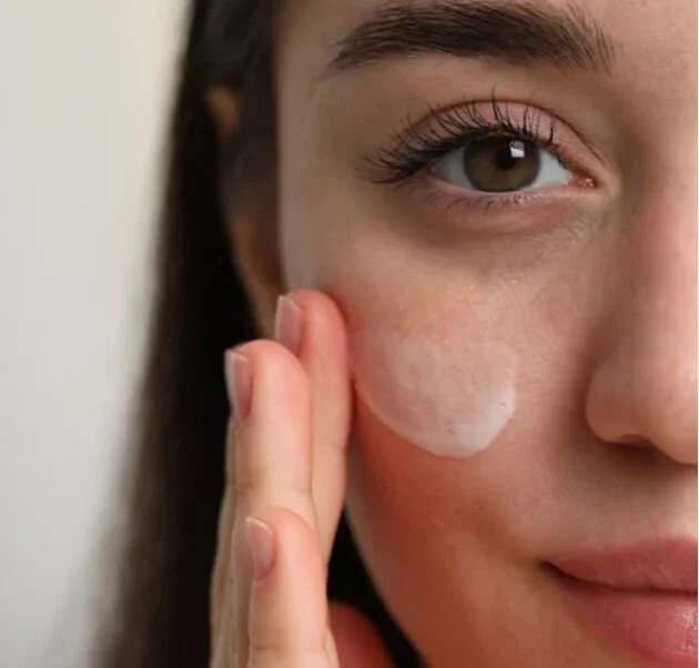 A woman applying skincare cream to her cheek.