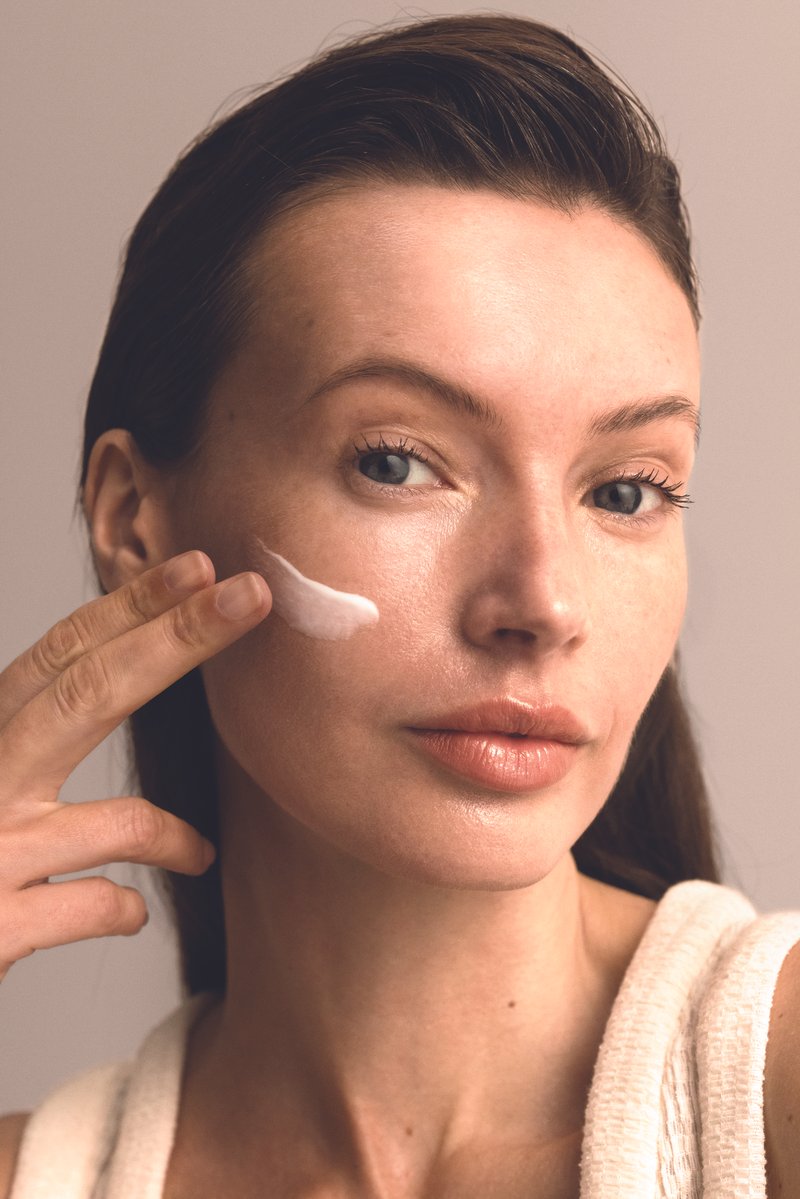 A woman with dark, long hair applying moisturiser to her cheek.