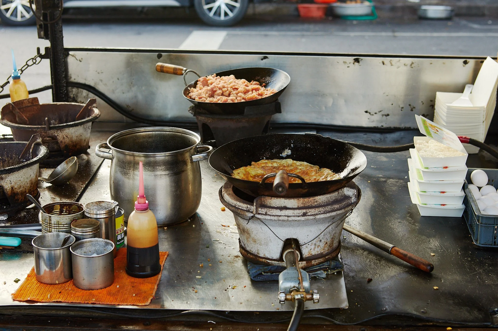 Street food stall cooking pancakes on a griddle, with condiments and containers on the table.