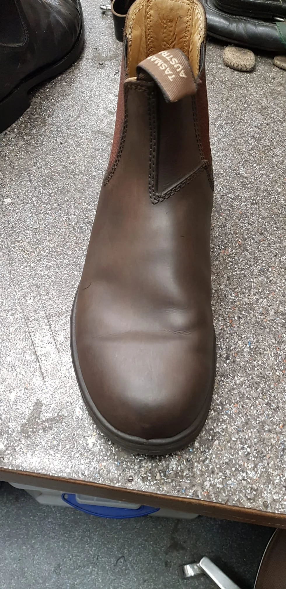 Ein brauner Lederstiefel auf einer Werkbank, umgeben von Werkzeugen und Steinen.