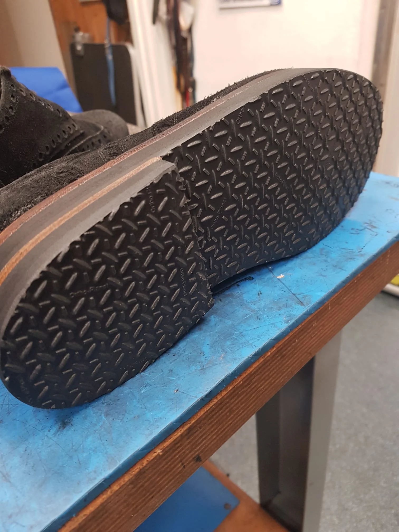 Nahaufnahme einer schwarzen Schuhsohle mit Muster, auf einem blauen und braunen Tisch.