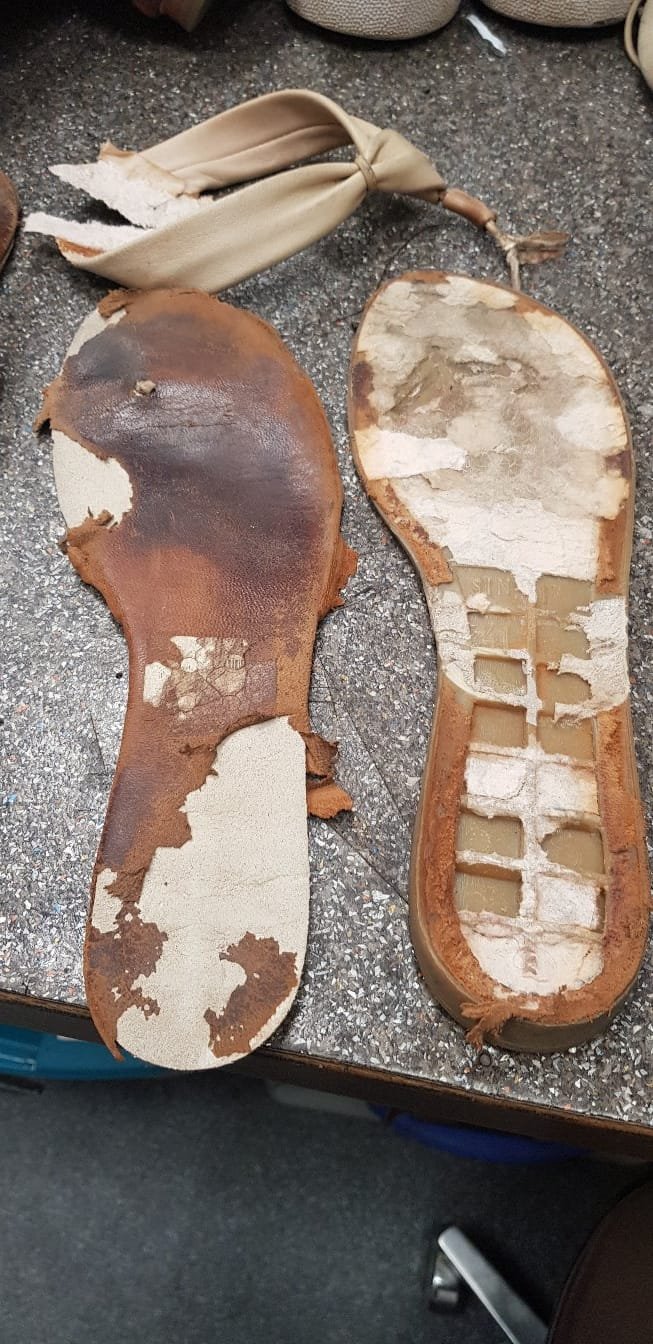 Abgefahrene und stark abgenutzte Leder- und Kunststoffsohlen von Kinderschuhen, die auf einem Tisch liegen.