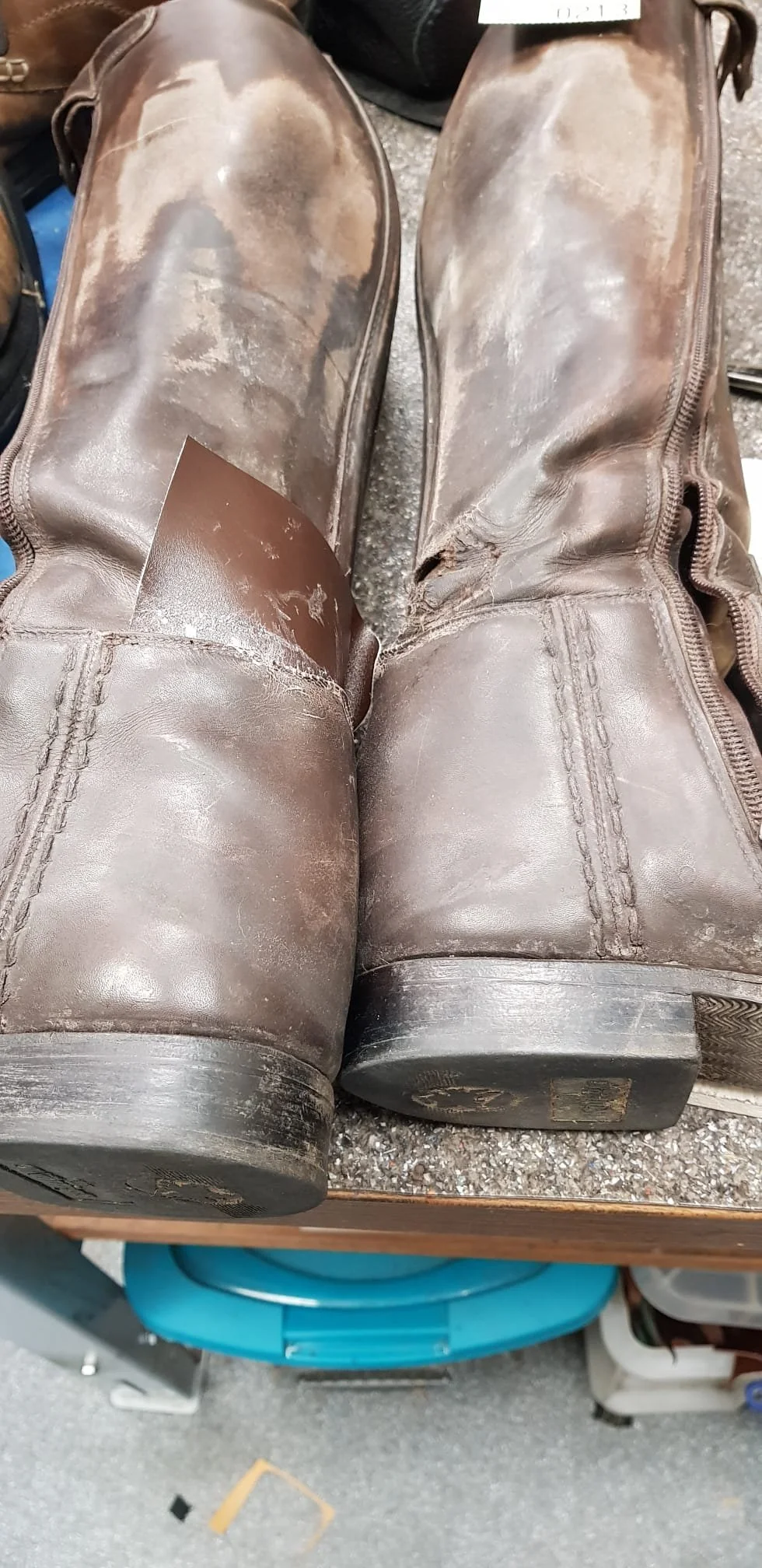 Ein Paar braune Lederstiefel mit sichtbar verschlissener Sohle und abgenutztem Schuhwerk liegt auf einem Tisch.