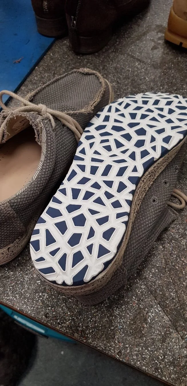 Ein verpflaidetes graues Schuh mit einem neuen in den Farben Schwarz und Weiß mit einem geometrischen Muster auf der Sohle, umgeben von anderen Schuhen auf einem Boden.