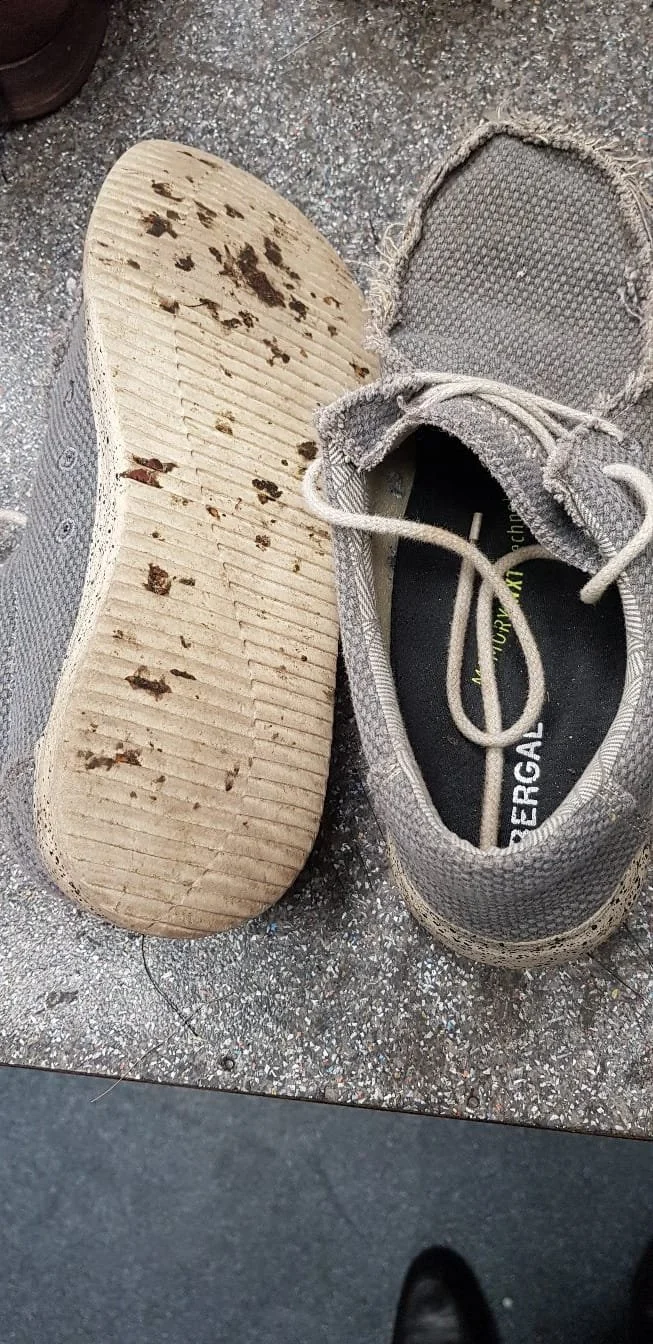 Ein Paar abgenutzte, graue Sportschuhe mit Schmutz am Boden, der auf einer grauen Asphaltfläche steht.