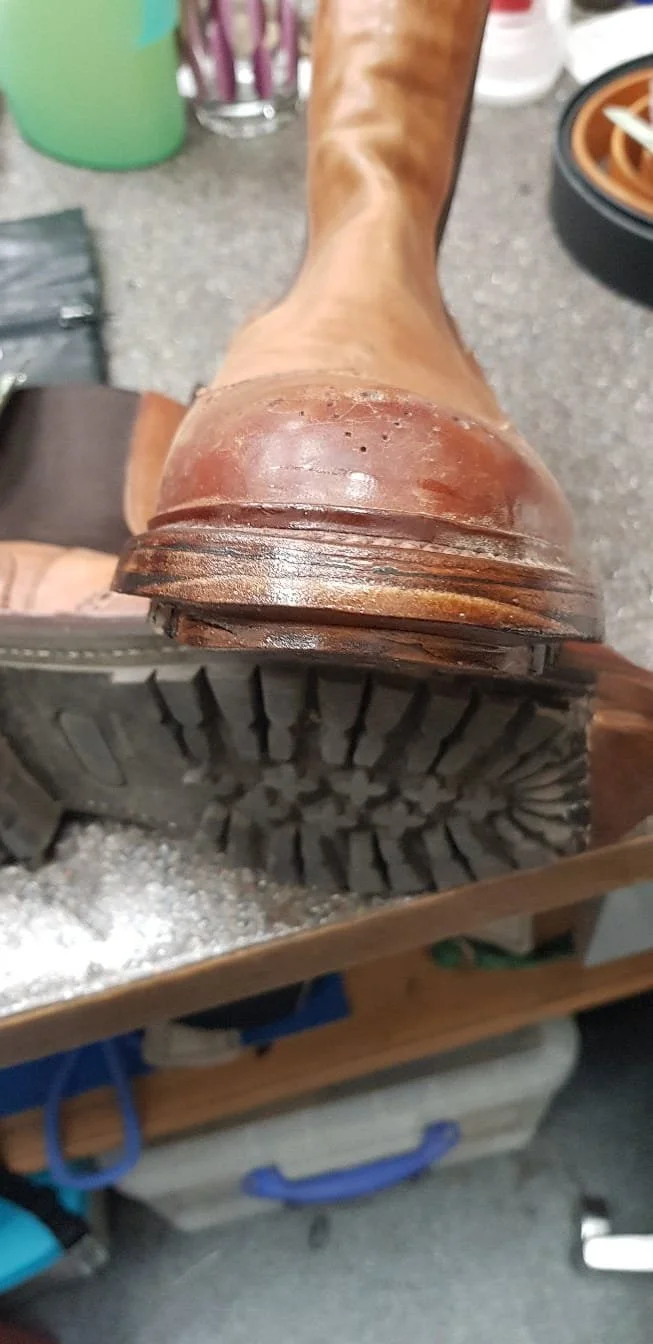 Nahaufnahme eines braunen Lederschuhs mit rutschfester Sohle, resting auf einem Tisch in einer Werkstatt oder einem Reparaturraum.