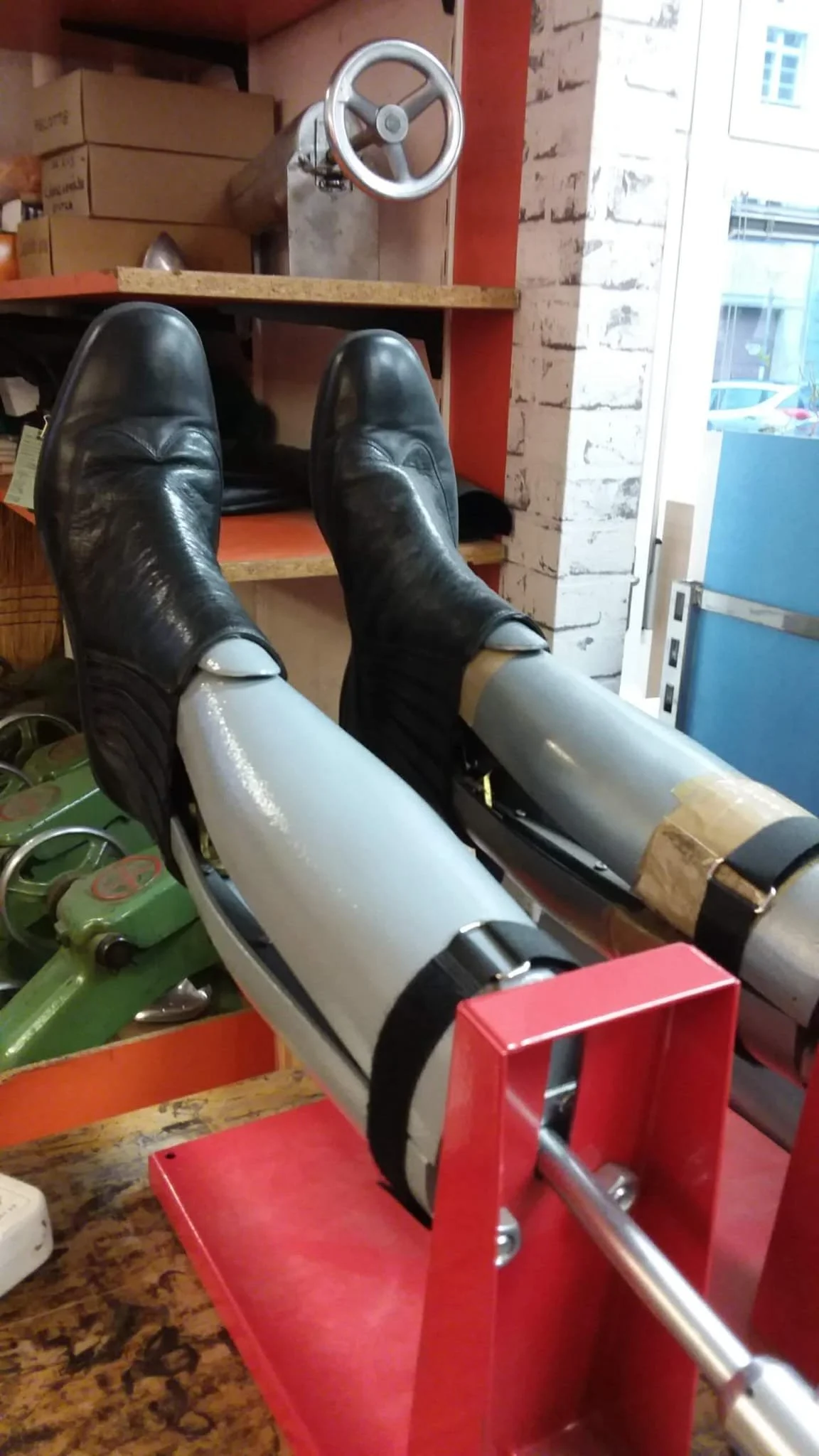 Eine Person trägt schwarze Schuhe und weiße Hosen, die auf einem roten Sofabett mit einem Spielzeugauto stehen, mit einem Industriestuhl und einer Bricksteinmauer im Hintergrund.