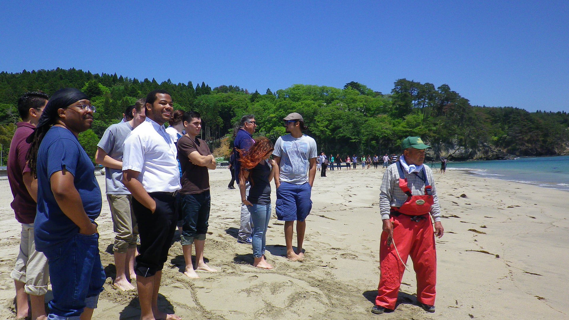 Aidan Hill among a group of people on a beach listening to a guide with red overalls during a tour.