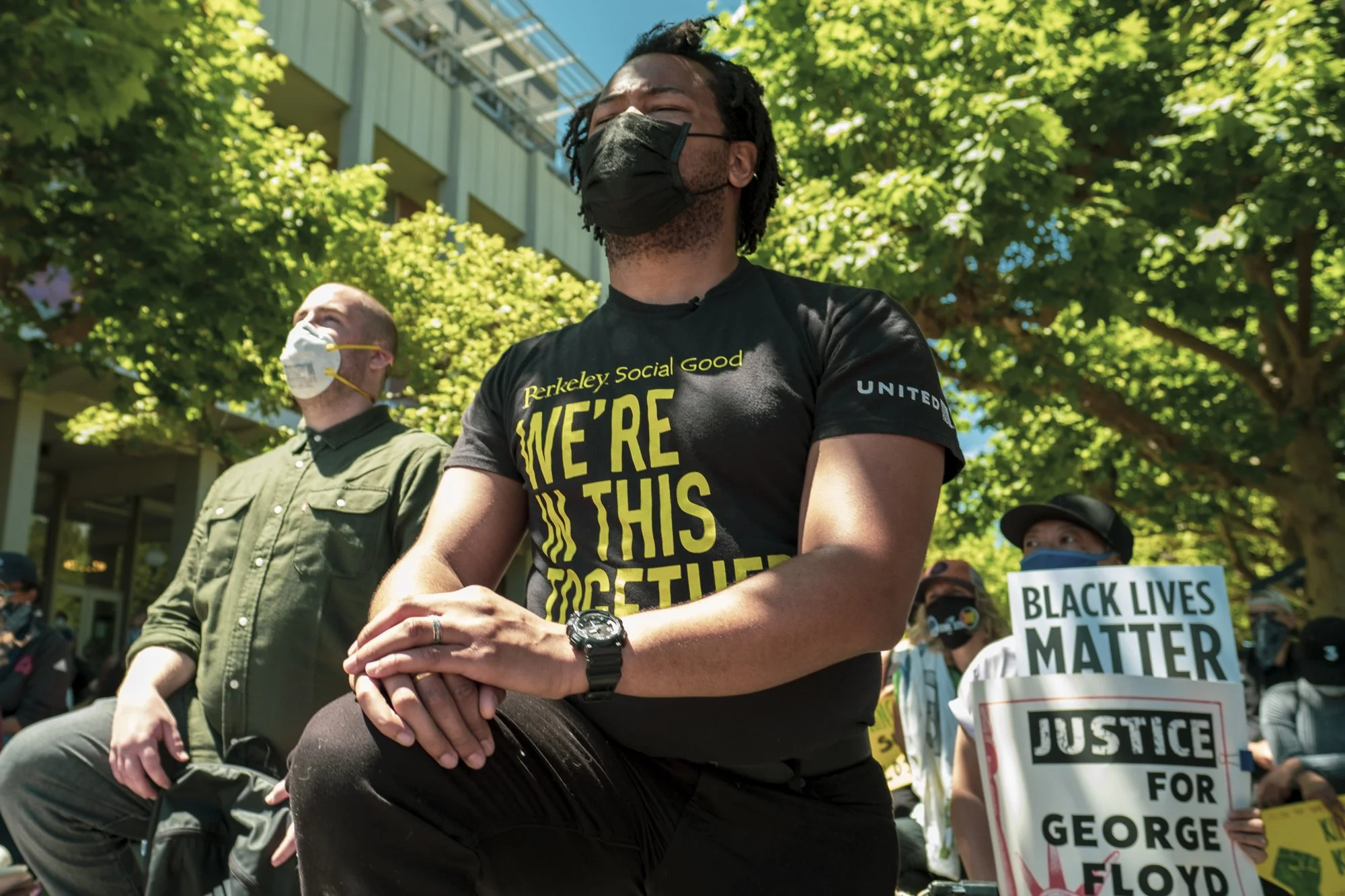 Aidan Hill among a group of people participating in a peaceful protest holding signs, one reading "Black Lives Matter" and another saying "Justice for George Floyd", with trees and a building in the background.