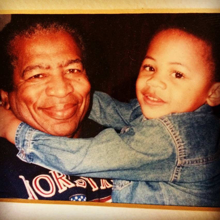 Aidan Hill's grandfather, a smiling older man, and a young Aidan wearing a denim jacket, hugging each other.