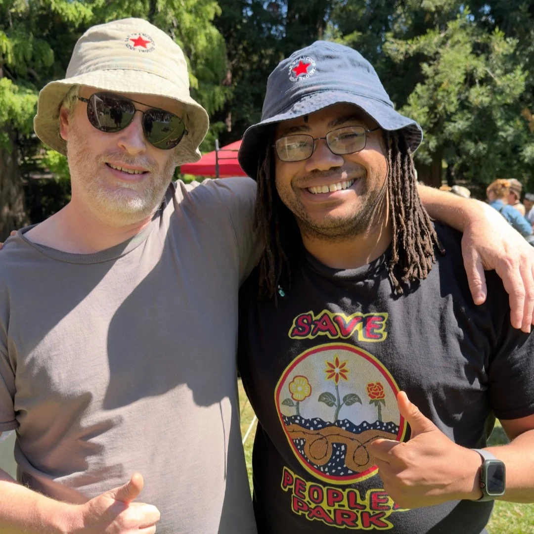 Aidan Hill and a composer Daniel Savio wearing San Francisco Mime Troupe hats at Live Oak Park in Berkeley